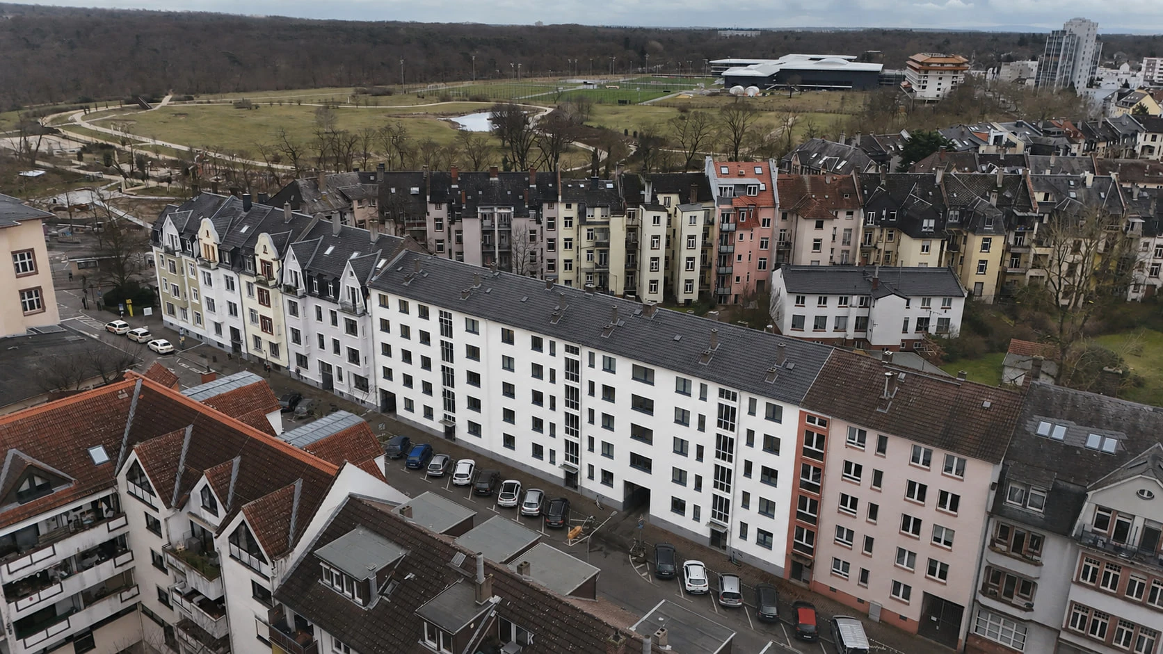 Das Projekt ENSEMBLE 27 aus der Luft über den Dächern des Viertels: die lange weiße Wohnzeile, dahinter Grünflächen und Sportanlagen bis zum Horizont.