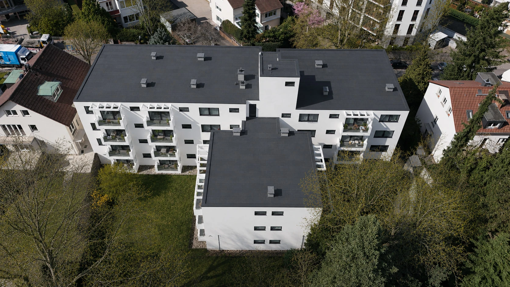 Die Dachlandschaft des Projekts SOUTH25 aus der Vogelperspektive: dunkle Flachdächer über den weißen Baukörpern, ringsum Gärten, Bäume und die Nachbarbebauung.