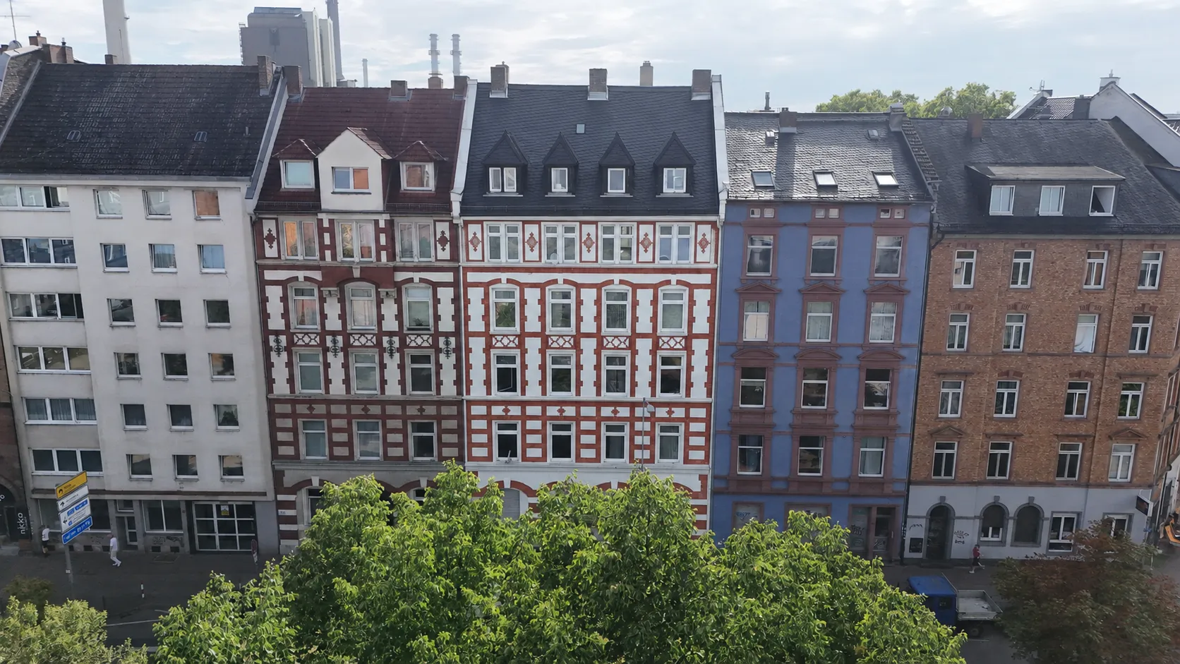 Luftaufnahme des Projekts HERITAGE 27: eine geschlossene Reihe von Gründerzeithäusern mit dunklen Dächern, darunter eine reich gegliederte Stuckfassade; im Hintergrund die Frankfurter Skyline, davor eine Baumreihe.