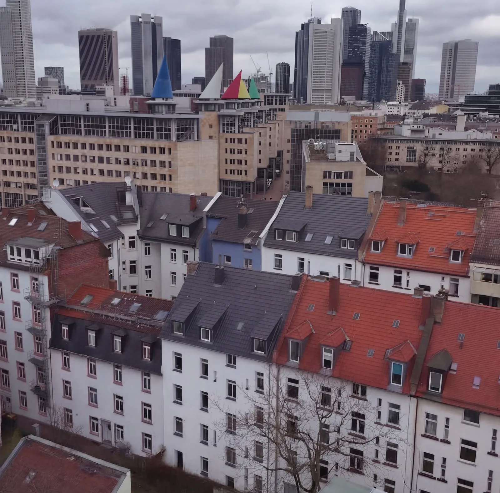 Blick über die Dächer des Viertels von HERITAGE 27 hinweg auf die Frankfurter Skyline: im Vordergrund die Altbaudächer mit Gauben und Schornsteinen, dahinter die Hochhäuser der Innenstadt.
